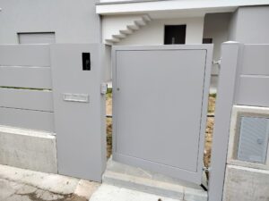 Cancello pedonale grigio chiaro in lamiera cieca installato presso un residence